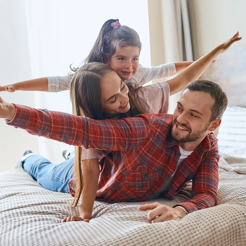 Familie mit Kind spielt auf einem Bett im Familienzimmer des Cinema City Hotels in Karlsruhe
