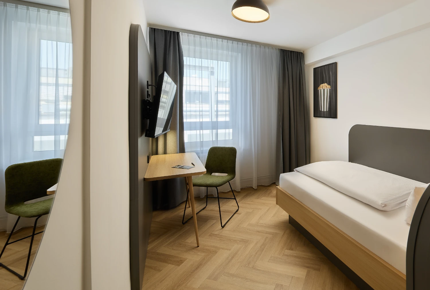 Modernes Einzelzimmer mit komfortablem Bett, Schreibtisch, Smart-TV und stilvoller Beleuchtung. Helle Farben, hochwertige Ausstattung und ein funktionaler Arbeitsplatz sorgen für einen angenehmen Aufenth