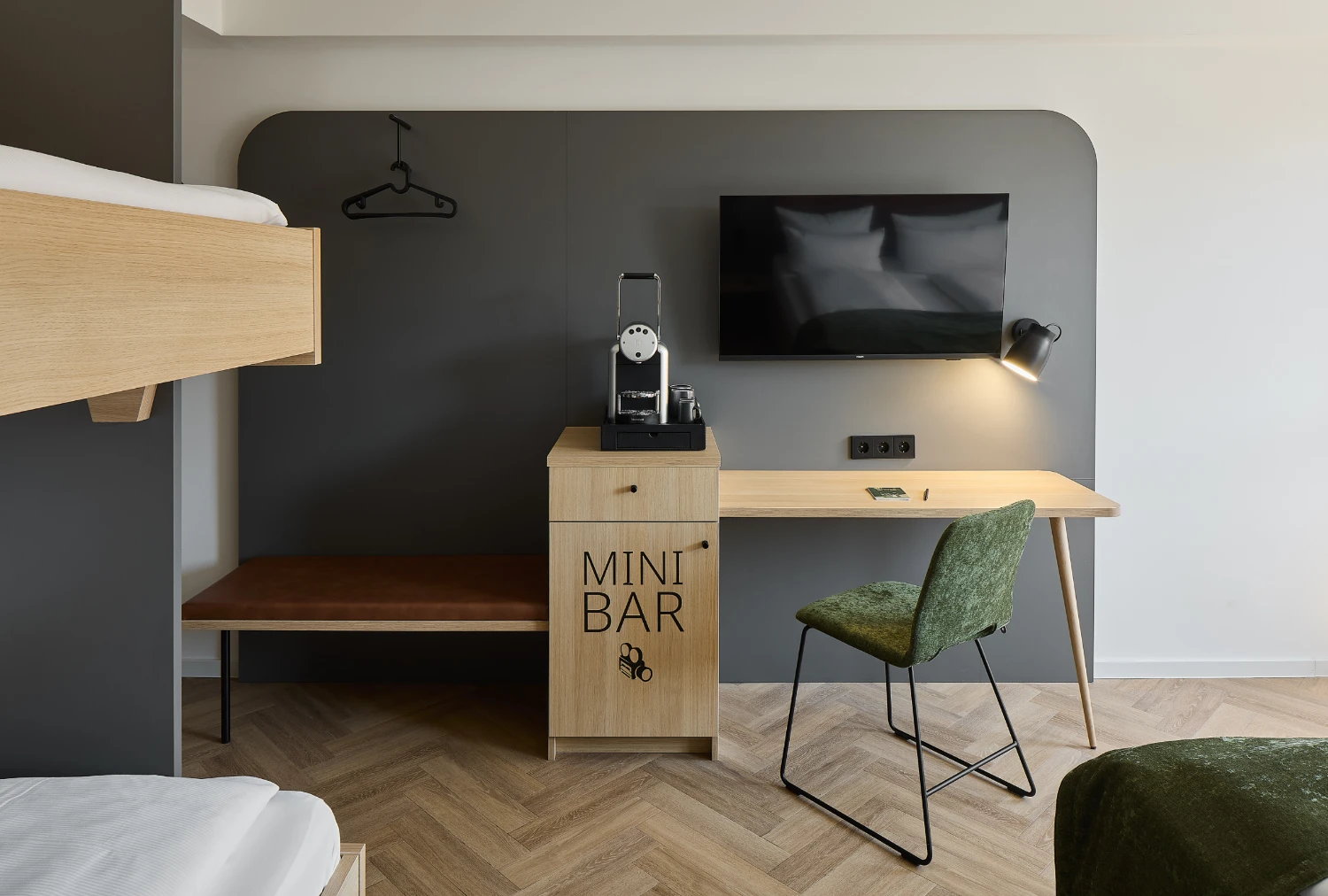 Moderner Arbeitsbereich im Familienzimmer mit Schreibtisch, Smart-TV, Kaffeemaschine und Minibar. Eine Sitzbank mit Garderobe sowie ein integriertes Etagenbett ergänzen die familienfreundliche Ausstattung.