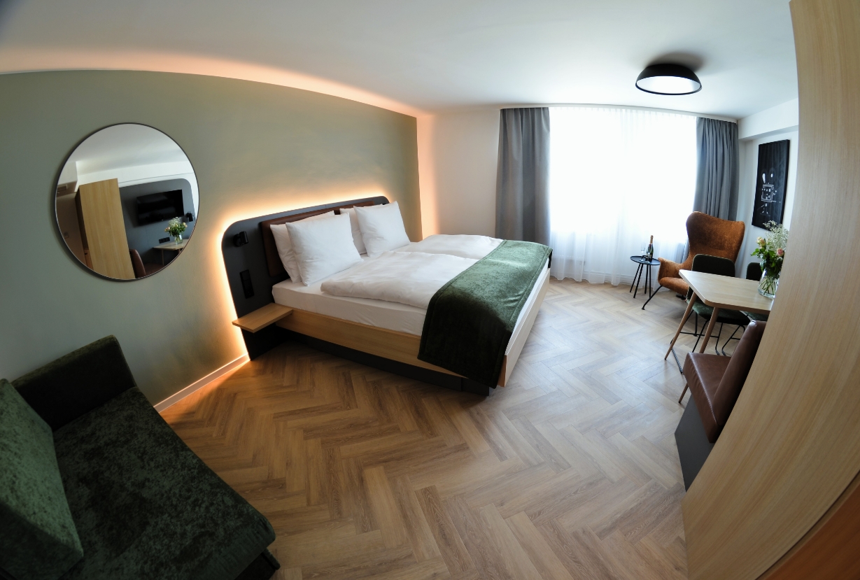 Apartment-Zimmer im Cinema City Hotel mit Doppelbett, modernem Design, Holzfußboden und Sitzbereich am Fenster.