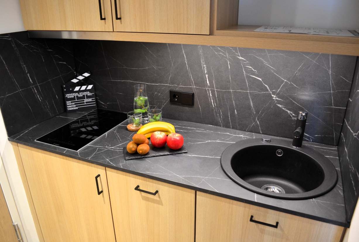 Moderne Küchenzeile im Apartment mit schwarzer Arbeitsplatte, Spüle, Obst und Gläsern im Cinema City Hotel.