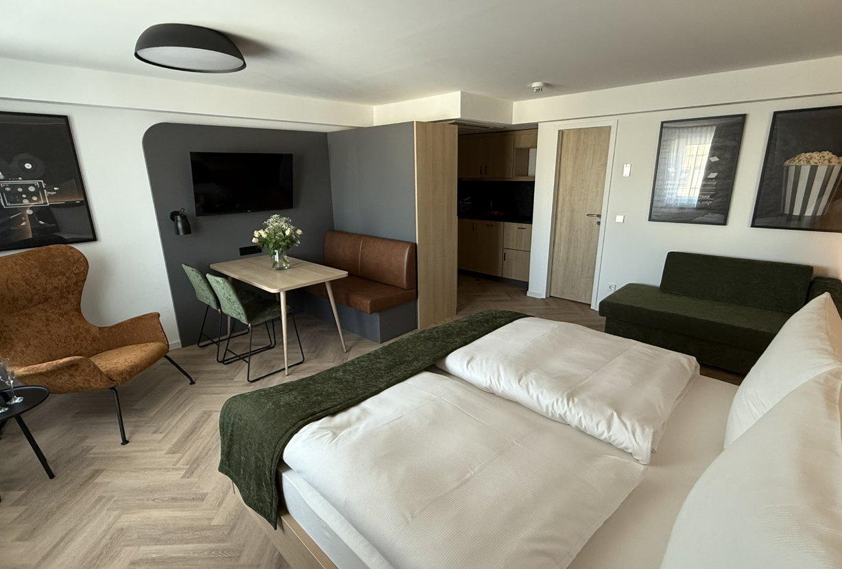 Apartment-Zimmer im Cinema City Hotel mit Doppelbett, Sitzecke, Esstisch, Fernseher und integrierter Küchenzeile.