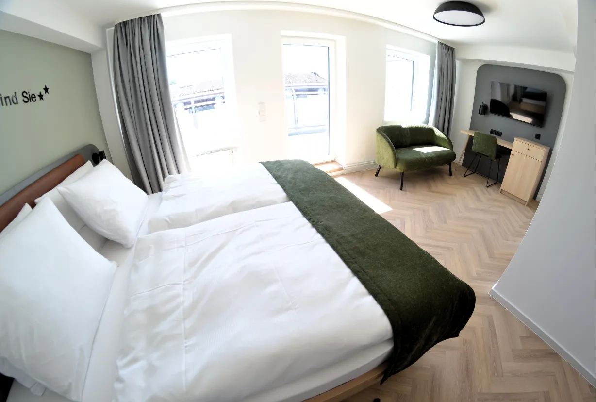 Helles Doppelzimmer mit Doppelbett, grünem Sofa und Schreibtisch im Cinema City Hotel