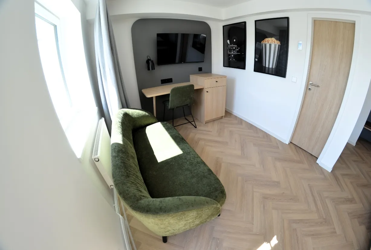 Modernes Doppelzimmer mit grünem Sofa, Schreibtisch und Wandfernseher im Cinema City Hotel