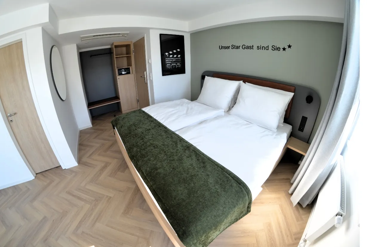 Doppelzimmer mit großem Bett, grünem Fußhocker und Wandtext