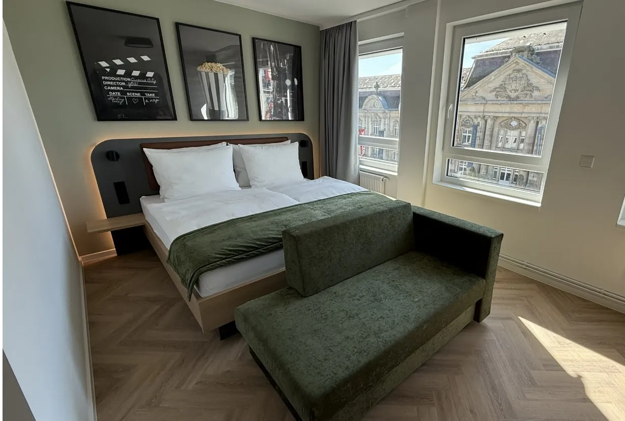 Dreibettzimmer mit Doppelbett, Schlafcouch und großem Fenster mit Stadtblick
