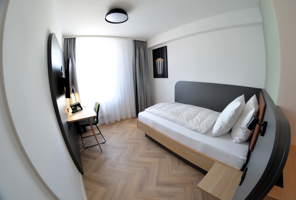 Ein stilvoll eingerichtetes Einzelzimmer mit Schreibtisch, TV und Tageslicht – ideal für Alleinreisende