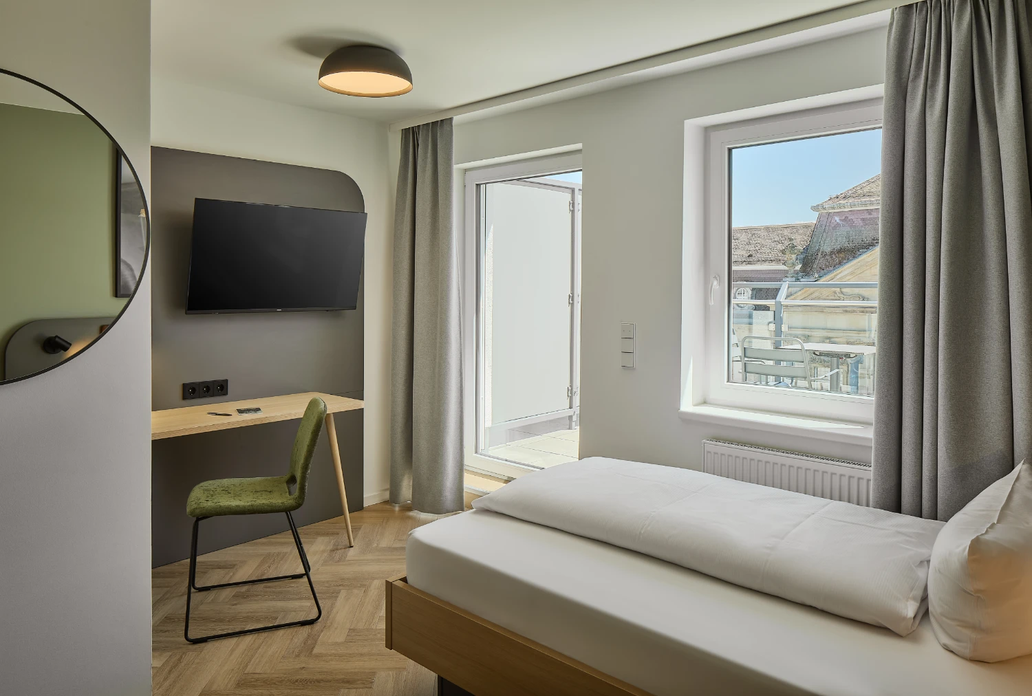 Modernes Einzelzimmer mit komfortablem Bett, Schreibtisch, Smart-TV und stilvoller Beleuchtung. Helle Farben, hochwertige Ausstattung und ein funktionaler Arbeitsplatz sorgen für einen angenehmen Aufenthalt.