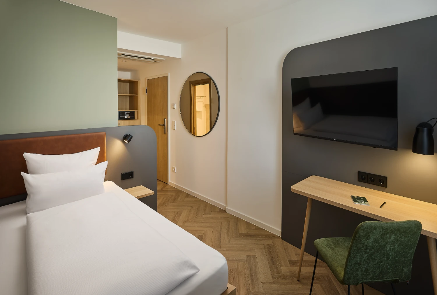 Modernes Einzelzimmer mit komfortablem Bett, Schreibtisch, Smart-TV und stilvoller Beleuchtung. Helle Farben, hochwertige Ausstattung und ein funktionaler Arbeitsplatz sorgen für einen angenehmen Aufenthalt.