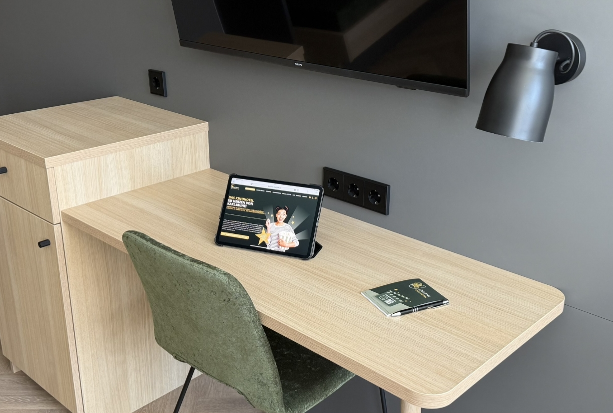 Moderner Schreibtisch im Familienzimmer mit Tablet, Infobroschüre und Wandfernseher im Cinema City Hotel