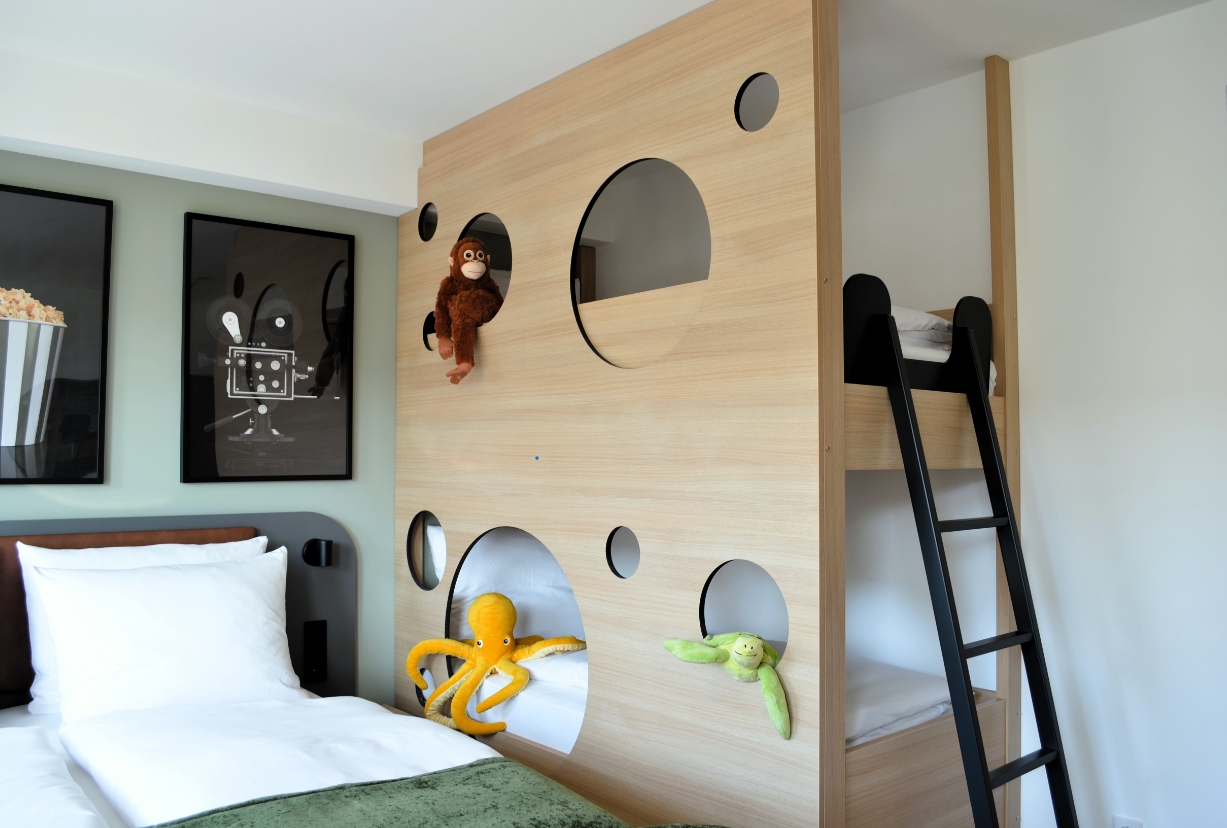 Detailansicht des Kinderstockbetts mit verspieltem Design, Kletterleiter und Stofftieren im Familienzimmer des Cinema City Hotels