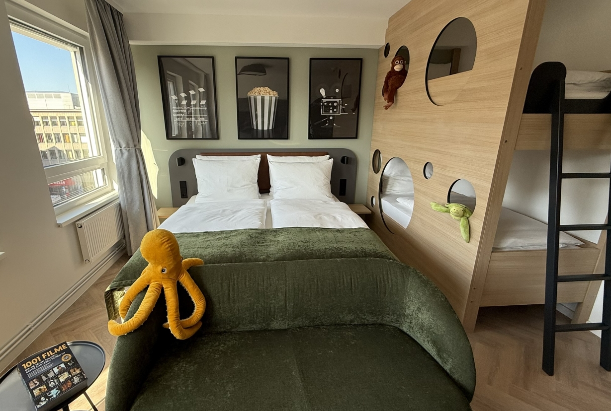 Helles Familienzimmer mit Doppelbett, Kinderstockbett, grünem Sofa und kinderfreundlicher Dekoration im Cinema City Hotel