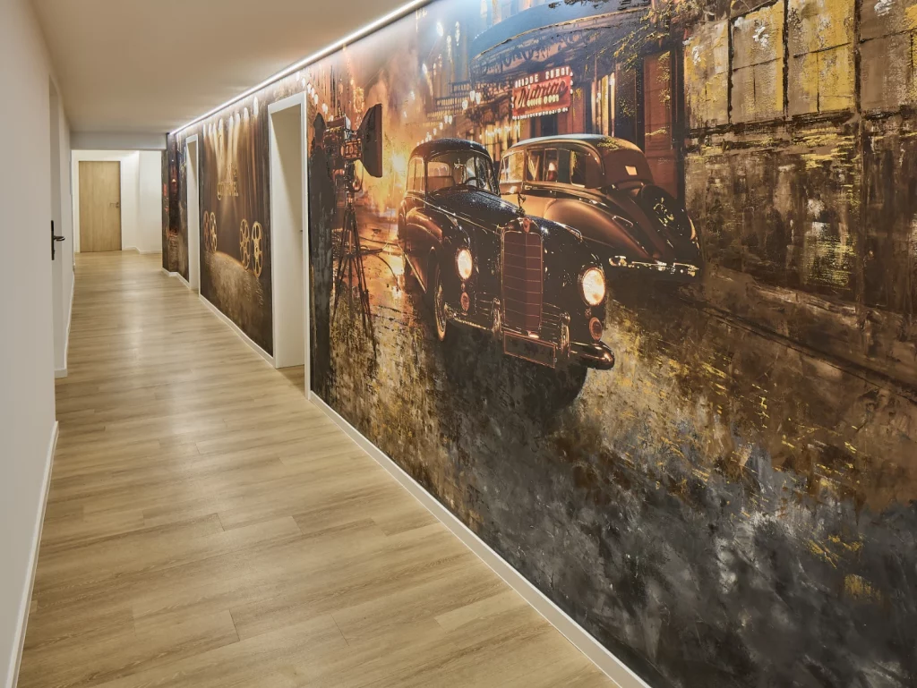 Thematisch gestalteter Hotelflur mit großflächigem Wandmotiv, rotem Teppich und beleuchteten Zimmerzugängen. Das moderne Design greift das Kino- und Filmkonzept des Hotels eindrucksvoll auf.