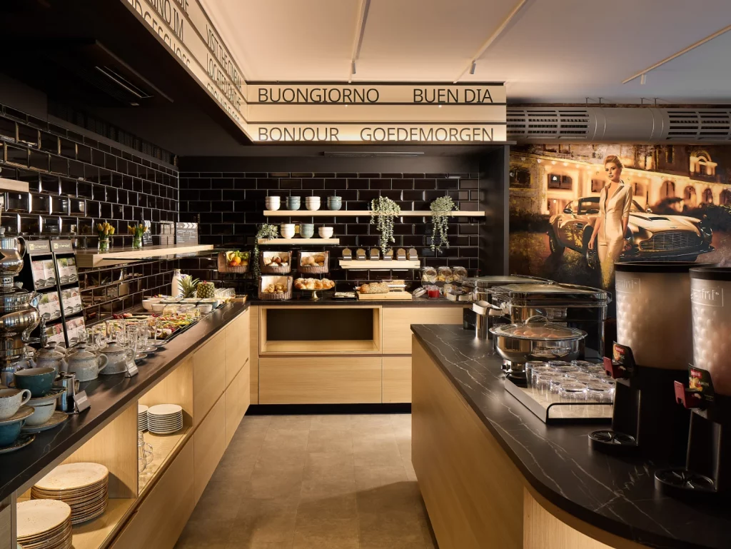 Modernes Frühstücksbuffet mit großer Auswahl an frischen Speisen, Backwaren, Obst, Kaffee und warmen Gerichten. Das stilvolle Ambiente mit internationalen Begrüßungen und offenen Buffetinseln lädt zu einem entspannten Start in den Tag ein.