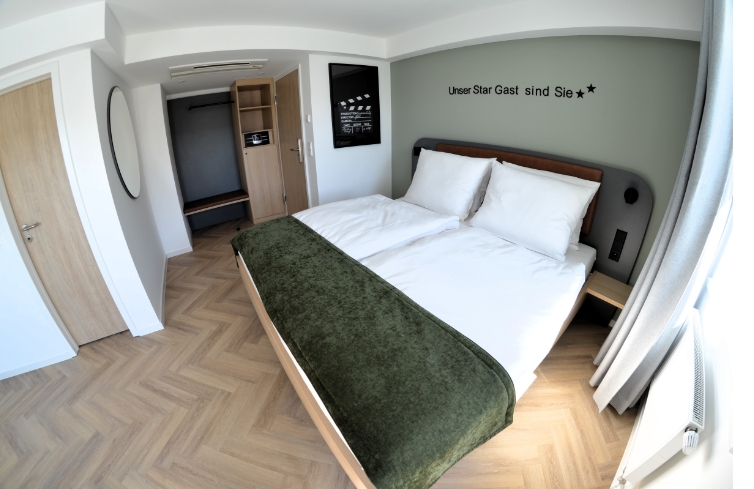 Modernes Zimmer mit Doppelbett, offenem Schrank und dem Motto „Unser Star Gast sind Sie“